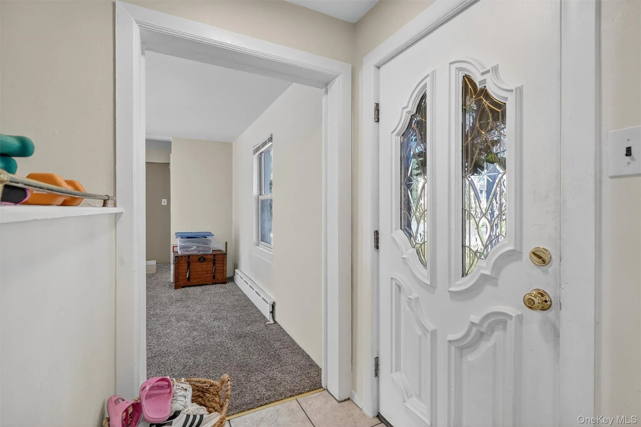 Foyer entrance featuring light carpet, plenty of natural light, a baseboard heating unit, and light tile patterned floors Foyer entrance featuring light carpet, plenty of natural light, a baseboard heating unit, and light tile patterned floors