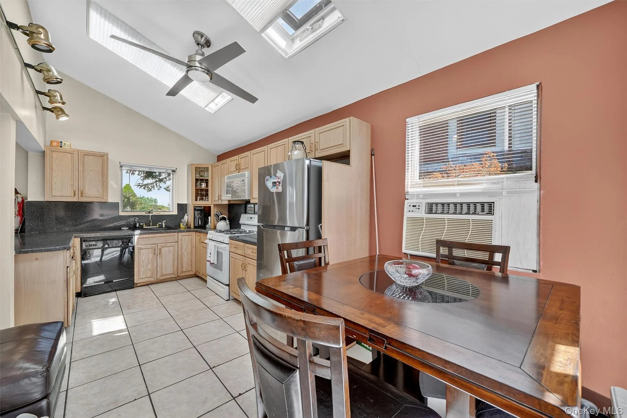 Kitchen with light brown cabinets, a skylight, light tile patterned floors, white appliances, and high vaulted ceiling Kitchen with light brown cabinets, a skylight, light tile patterned floors, white appliances, and high vaulted ceiling