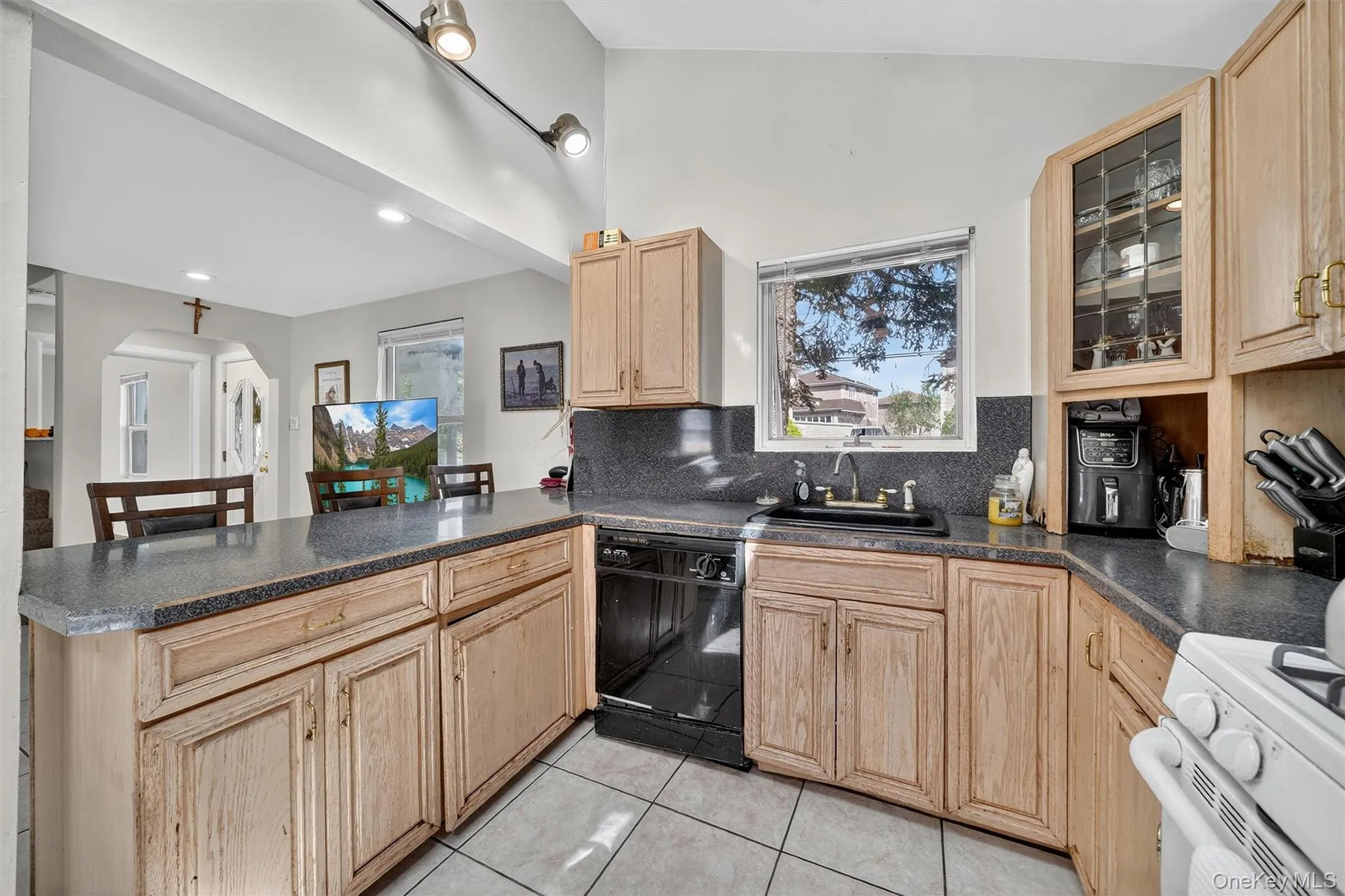 Kitchen featuring dark countertops, light brown cabinets, white range oven, a peninsula, and black dishwasher Kitchen featuring dark countertops, light brown cabinets, white range oven, a peninsula, and black dishwasher
