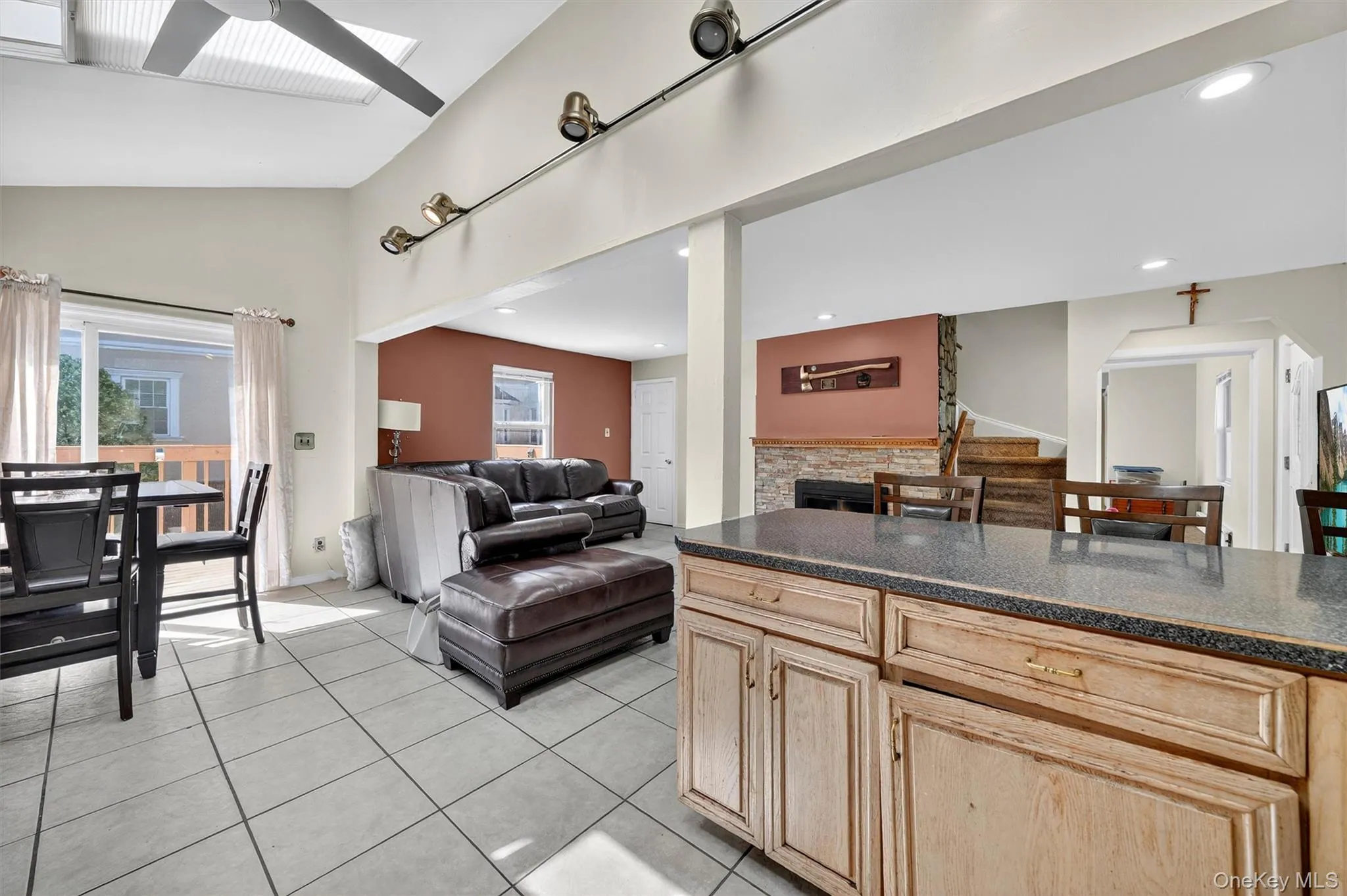 Kitchen with light brown cabinetry, dark stone countertops, light tile patterned floors, open floor plan, and a skylight Kitchen with light brown cabinetry, dark stone countertops, light tile patterned floors, open floor plan, and a skylight