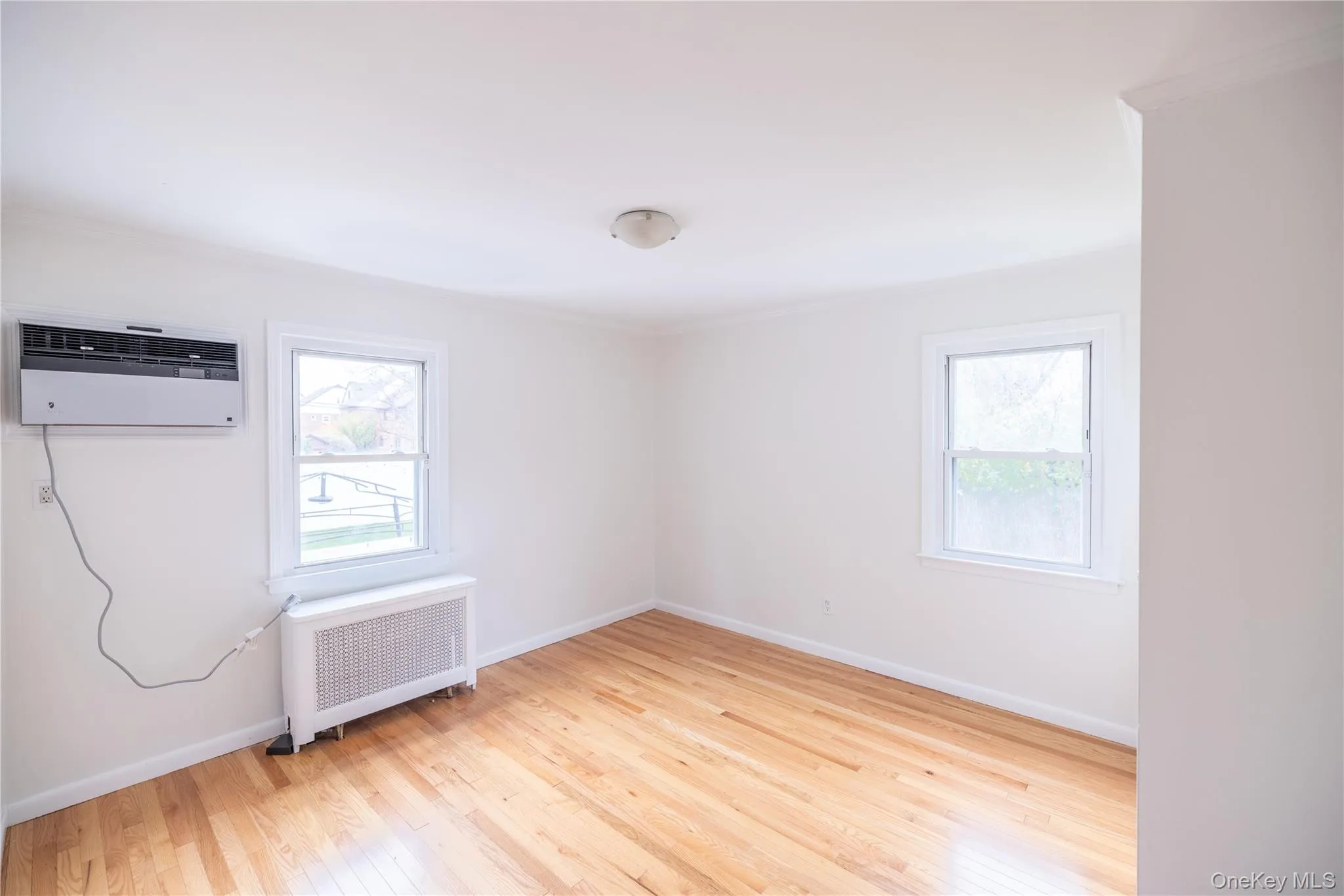 Empty room featuring radiator heating unit, light wood-type flooring, ornamental molding, and a wall unit AC Empty room featuring radiator heating unit, light wood-type flooring, ornamental molding, and a wall unit AC