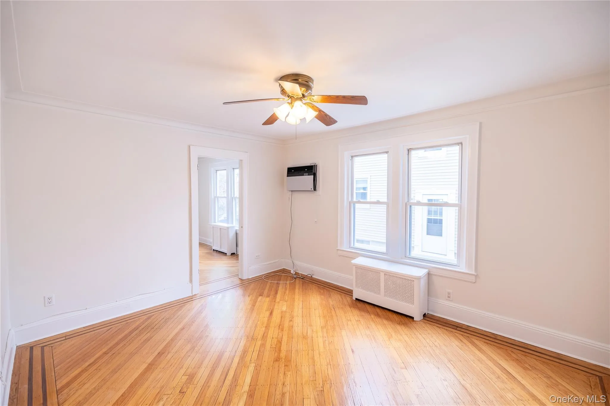 Spare room featuring radiator, wood finished floors, ornamental molding, a ceiling fan, and an AC wall unit Spare room featuring radiator, wood finished floors, ornamental molding, a ceiling fan, and an AC wall unit