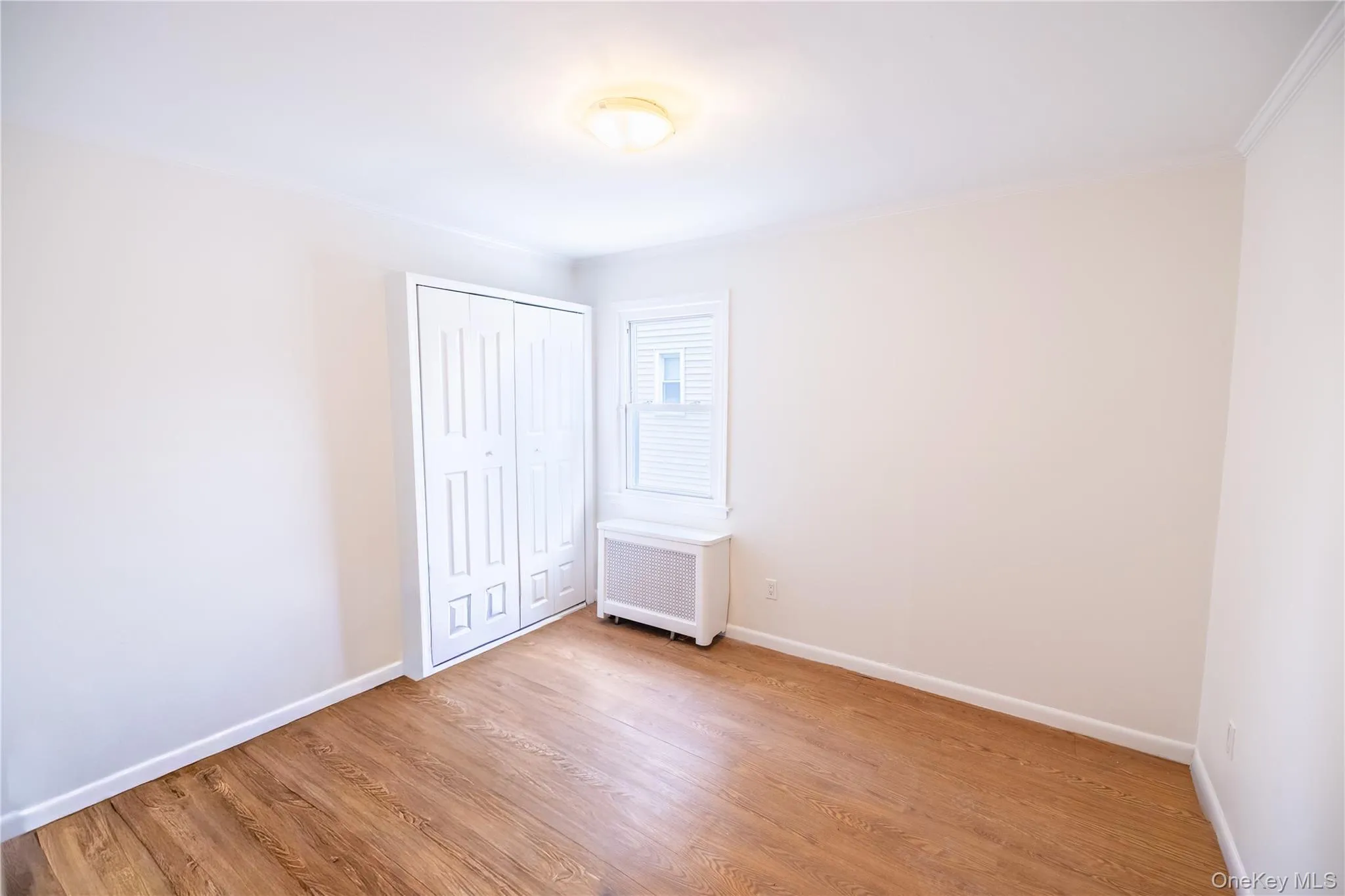 Unfurnished bedroom with light wood-style floors, a closet, radiator, and ornamental molding Unfurnished bedroom with light wood-style floors, a closet, radiator, and ornamental molding