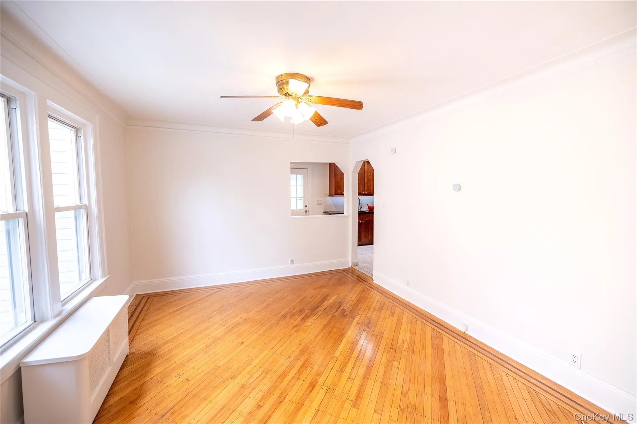 Spare room with hardwood / wood-style floors, arched walkways, ornamental molding, ceiling fan, and radiator Spare room with hardwood / wood-style floors, arched walkways, ornamental molding, ceiling fan, and radiator