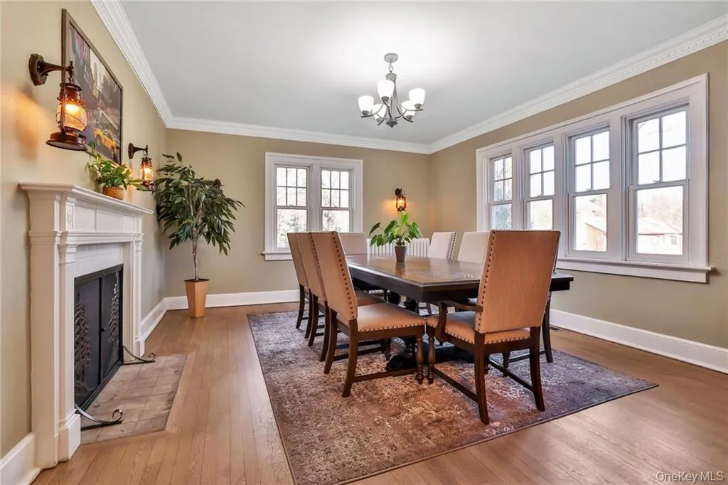 Dining space featuring light wood-style flooring, a fireplace with flush hearth, ornamental molding, and a chandelier Dining space featuring light wood-style flooring, a fireplace with flush hearth, ornamental molding, and a chandelier