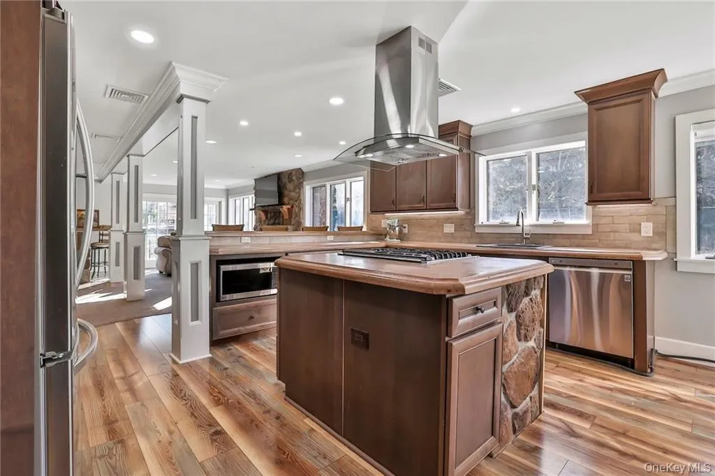 Kitchen with appliances with stainless steel finishes, island range hood, dark brown cabinets, tasteful backsplash, and a center island Kitchen with appliances with stainless steel finishes, island range hood, dark brown cabinets, tasteful backsplash, and a center island