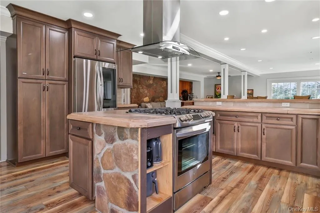 Kitchen featuring stainless steel appliances, wood counters, island range hood, light wood-type flooring, and a kitchen island Kitchen featuring stainless steel appliances, wood counters, island range hood, light wood-type flooring, and a kitchen island
