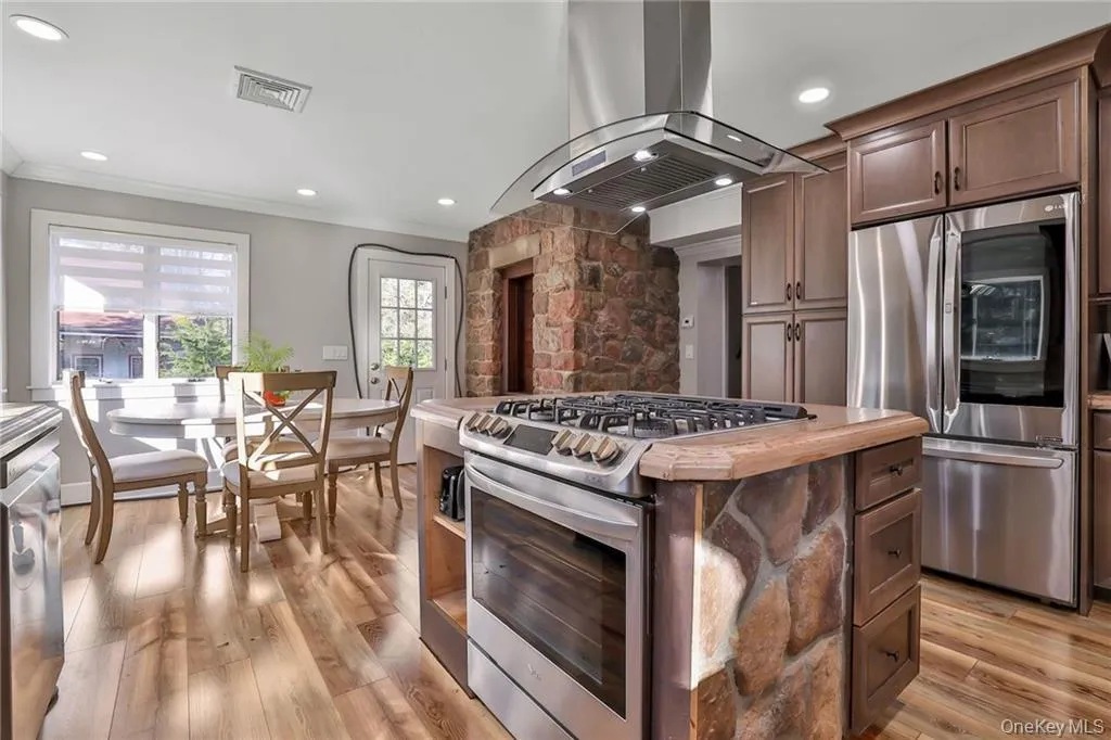 Kitchen featuring stainless steel appliances, island range hood, dark brown cabinetry, light wood-style floors, and a center island Kitchen featuring stainless steel appliances, island range hood, dark brown cabinetry, light wood-style floors, and a center island