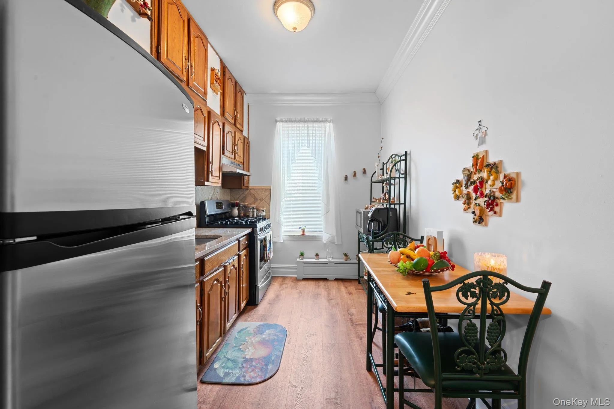 Kitchen featuring appliances with stainless steel finishes, crown molding, brown cabinets, light wood finished floors, and decorative backsplash Kitchen featuring appliances with stainless steel finishes, crown molding, brown cabinets, light wood finished floors, and decorative backsplash