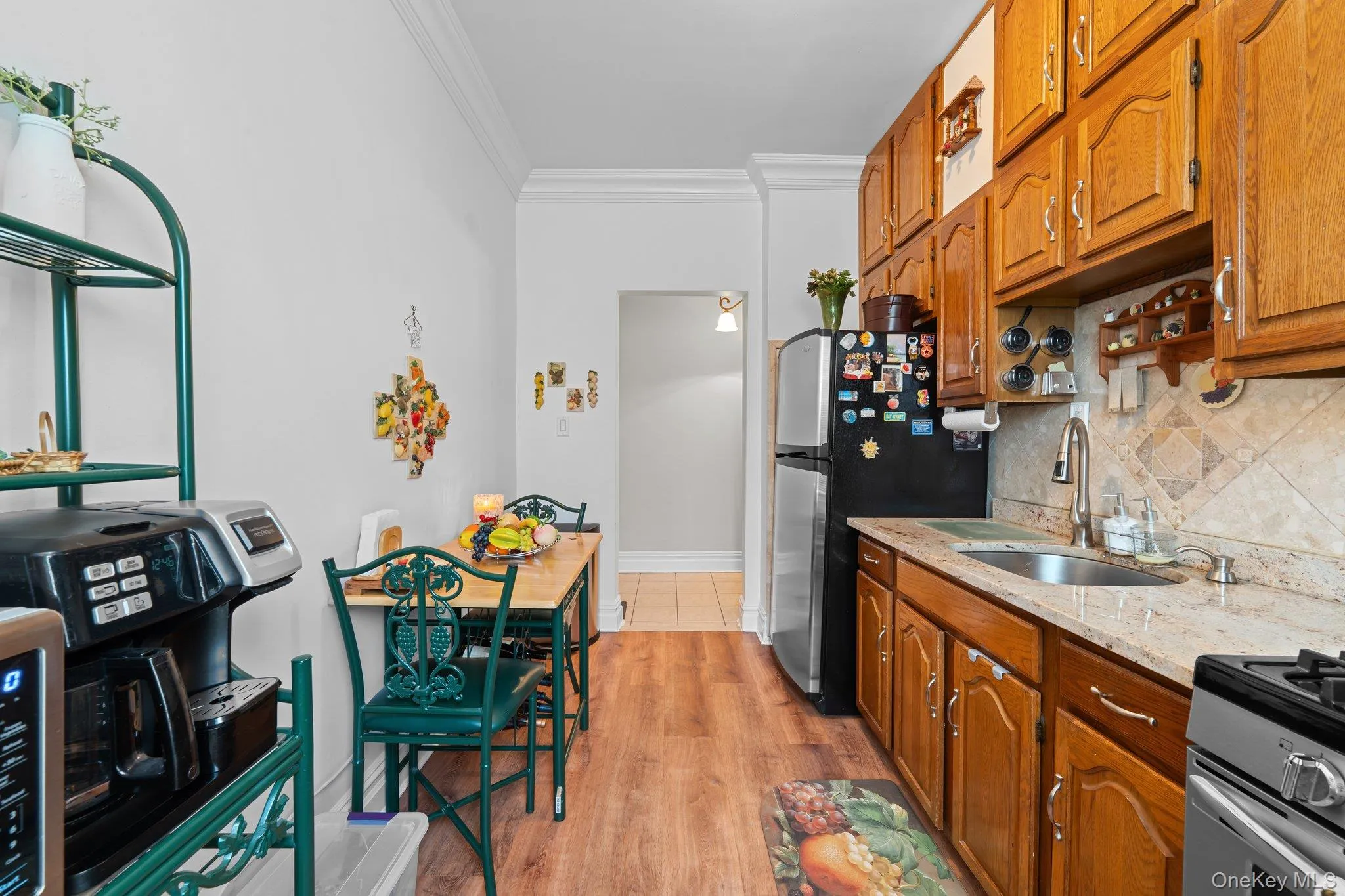 Kitchen featuring brown cabinetry, ornamental molding, light stone counters, light wood finished floors, and decorative backsplash Kitchen featuring brown cabinetry, ornamental molding, light stone counters, light wood finished floors, and decorative backsplash
