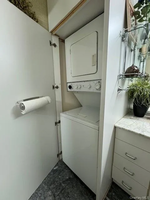 Washroom featuring dark tile patterned flooring and stacked washer / dryer Washroom featuring dark tile patterned flooring and stacked washer / dryer