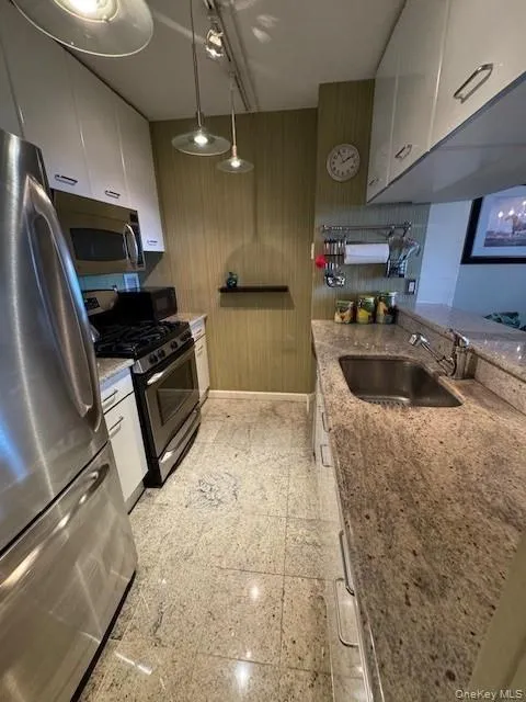 Kitchen with stainless steel appliances, light tile patterned floors, sink, white cabinetry, and light stone counters Kitchen with stainless steel appliances, light tile patterned floors, sink, white cabinetry, and light stone counters