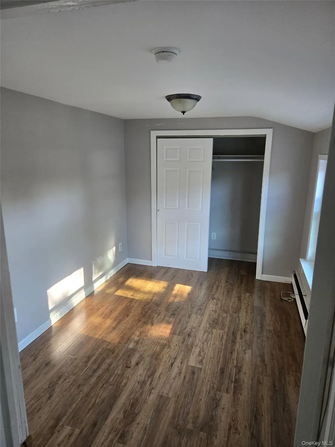 Unfurnished bedroom featuring a closet, dark wood-style floors, and a baseboard heating unit Unfurnished bedroom featuring a closet, dark wood-style floors, and a baseboard heating unit