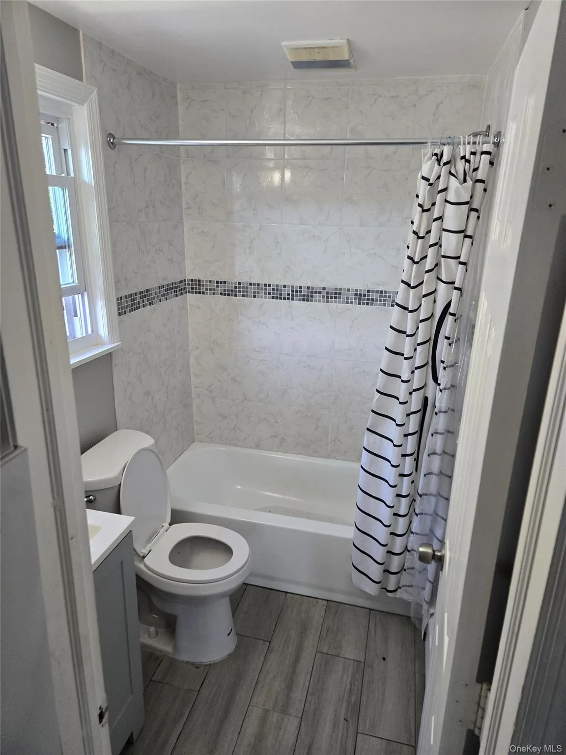 Full bathroom with shower / bathtub combination with curtain, vanity, and wood finish floors Full bathroom with shower / bathtub combination with curtain, vanity, and wood finish floors