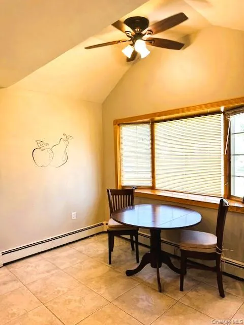 Dining area with a baseboard heating unit, lofted ceiling, a ceiling fan, and light tile patterned floors Dining area with a baseboard heating unit, lofted ceiling, a ceiling fan, and light tile patterned floors