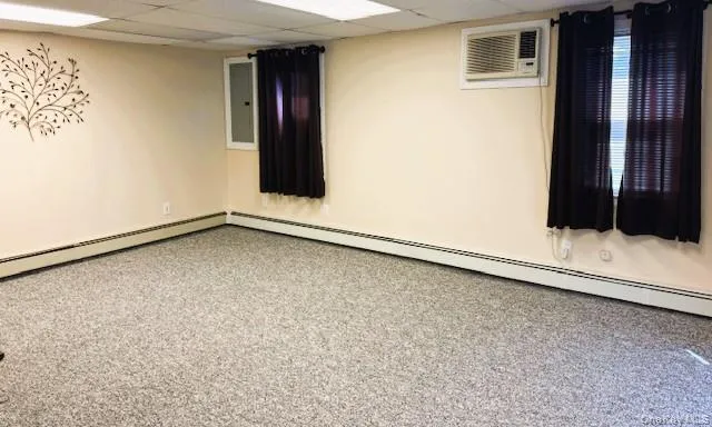 Empty room featuring a drop ceiling, baseboard heating, a wall unit AC, and carpet flooring Empty room featuring a drop ceiling, baseboard heating, a wall unit AC, and carpet flooring
