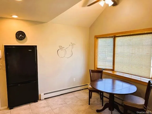 Dining room with a baseboard heating unit, light tile patterned flooring, vaulted ceiling, and a ceiling fan Dining room with a baseboard heating unit, light tile patterned flooring, vaulted ceiling, and a ceiling fan