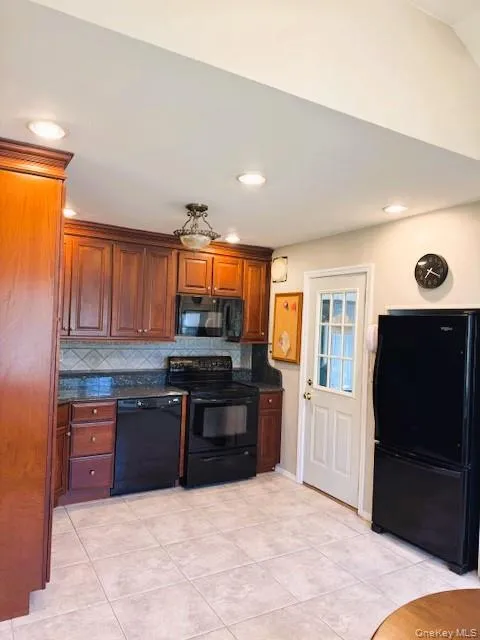 Kitchen with decorative backsplash, black appliances, light tile patterned floors, recessed lighting, and dark stone countertops Kitchen with decorative backsplash, black appliances, light tile patterned floors, recessed lighting, and dark stone countertops