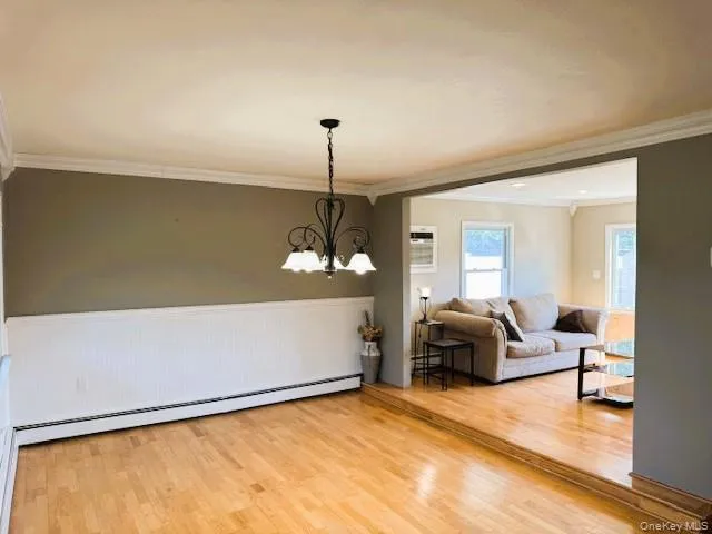 Dining space with crown molding, light wood-type flooring, a chandelier, baseboard heating, and wainscoting Dining space with crown molding, light wood-type flooring, a chandelier, baseboard heating, and wainscoting