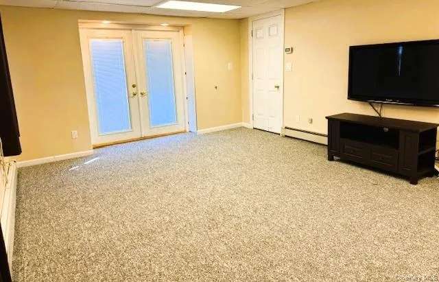 Unfurnished living room featuring french doors, light colored carpet, a drop ceiling, and a baseboard heating unit Unfurnished living room featuring french doors, light colored carpet, a drop ceiling, and a baseboard heating unit