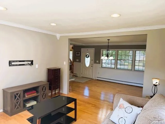 Living room featuring light wood-style flooring, a baseboard radiator, ornamental molding, recessed lighting, and stairs Living room featuring light wood-style flooring, a baseboard radiator, ornamental molding, recessed lighting, and stairs