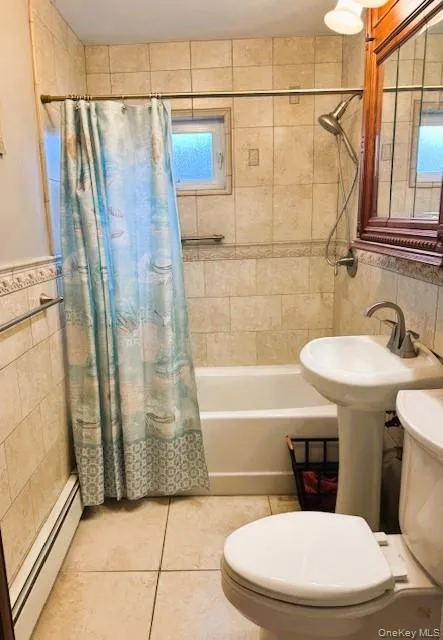 Full bathroom featuring tile walls, shower / bath combination with curtain, baseboard heating, light tile patterned floors, and a wainscoted wall Full bathroom featuring tile walls, shower / bath combination with curtain, baseboard heating, light tile patterned floors, and a wainscoted wall
