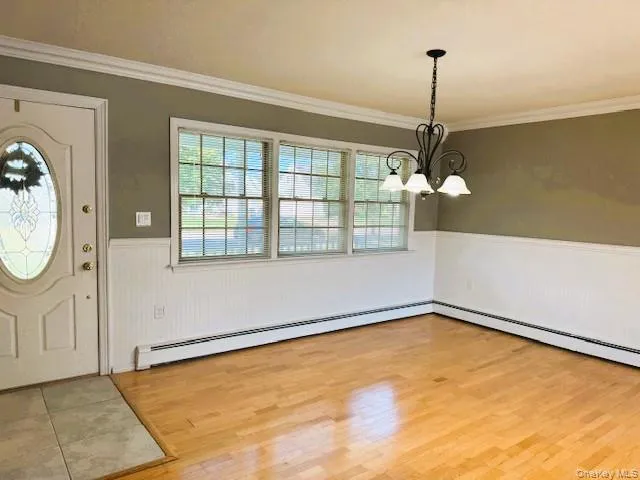 Entryway with a wainscoted wall, a chandelier, crown molding, light wood-type flooring, and a baseboard heating unit Entryway with a wainscoted wall, a chandelier, crown molding, light wood-type flooring, and a baseboard heating unit