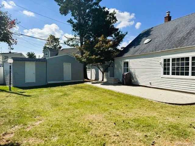Back of property featuring a lawn, a patio, an outdoor structure, roof with shingles, and a chimney Back of property featuring a lawn, a patio, an outdoor structure, roof with shingles, and a chimney