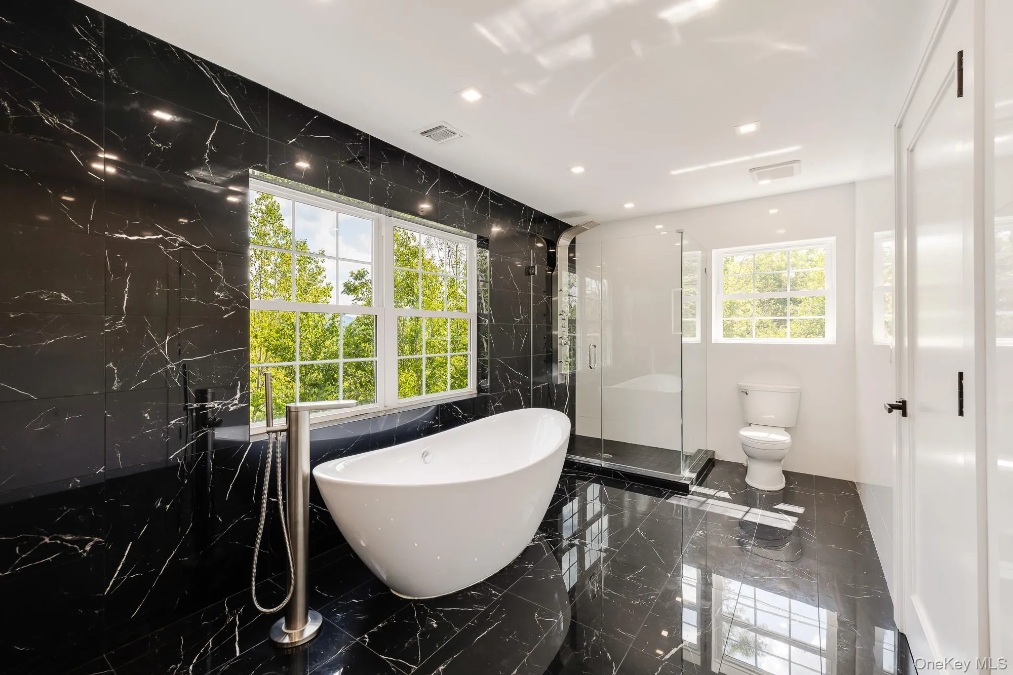 Full bath featuring a freestanding tub, toilet, a shower stall, visible vents, and marble finish floor Full bath featuring a freestanding tub, toilet, a shower stall, visible vents, and marble finish floor