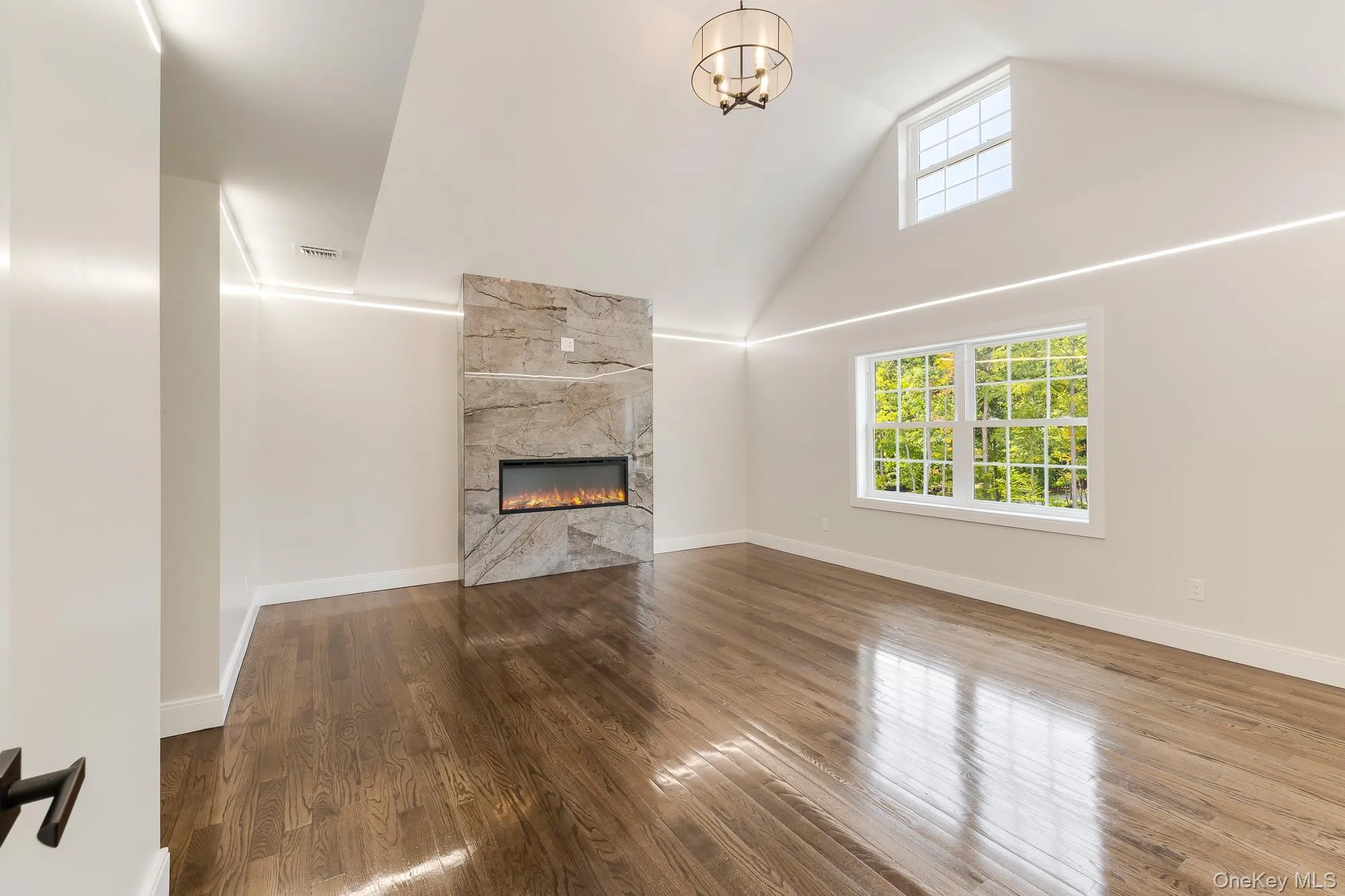 Unfurnished living room featuring high vaulted ceiling, wood finished floors, a fireplace, and a healthy amount of sunlight Unfurnished living room featuring high vaulted ceiling, wood finished floors, a fireplace, and a healthy amount of sunlight