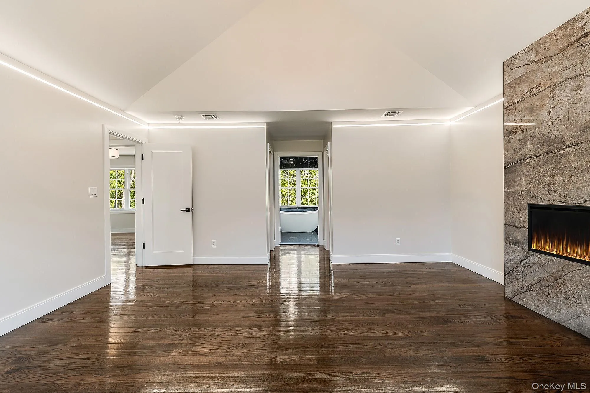 Unfurnished living room featuring wood finished floors, high vaulted ceiling, a fireplace, and a wealth of natural light Unfurnished living room featuring wood finished floors, high vaulted ceiling, a fireplace, and a wealth of natural light