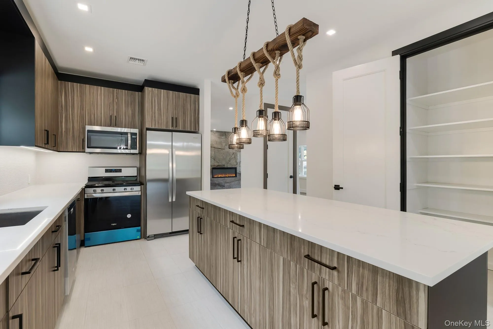 Kitchen featuring modern cabinets, light stone counters, a high end fireplace, and stainless steel appliances Kitchen featuring modern cabinets, light stone counters, a high end fireplace, and stainless steel appliances