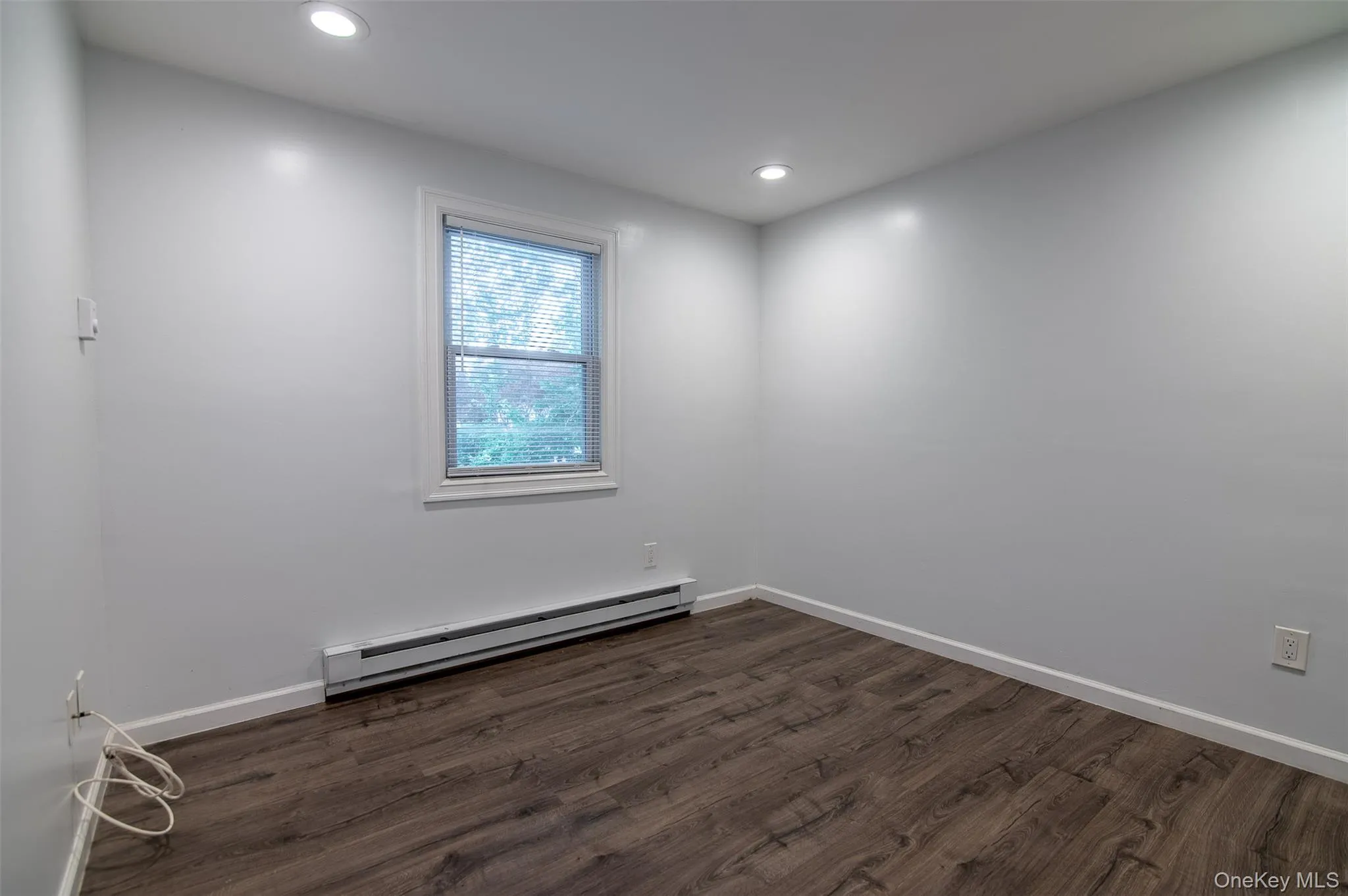 Empty room featuring a baseboard heating unit, dark wood-type flooring, and recessed lighting Empty room featuring a baseboard heating unit, dark wood-type flooring, and recessed lighting