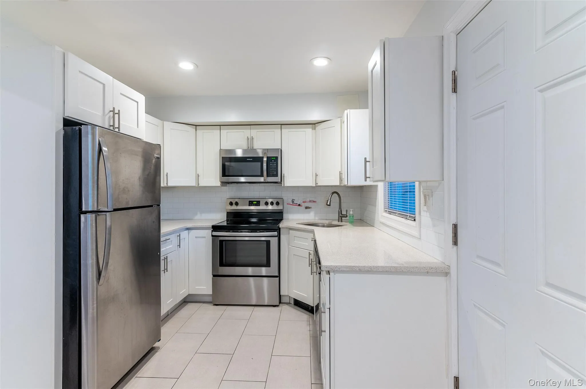 Kitchen featuring appliances with stainless steel finishes, light stone counters, white cabinetry, backsplash, and light tile patterned floors Kitchen featuring appliances with stainless steel finishes, light stone counters, white cabinetry, backsplash, and light tile patterned floors