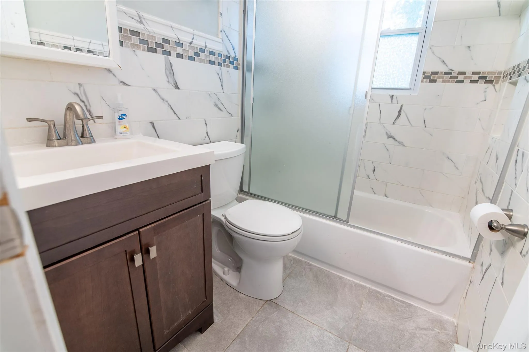 Bathroom featuring enclosed tub / shower combo, vanity, decorative backsplash, light tile patterned flooring, and tile walls Bathroom featuring enclosed tub / shower combo, vanity, decorative backsplash, light tile patterned flooring, and tile walls