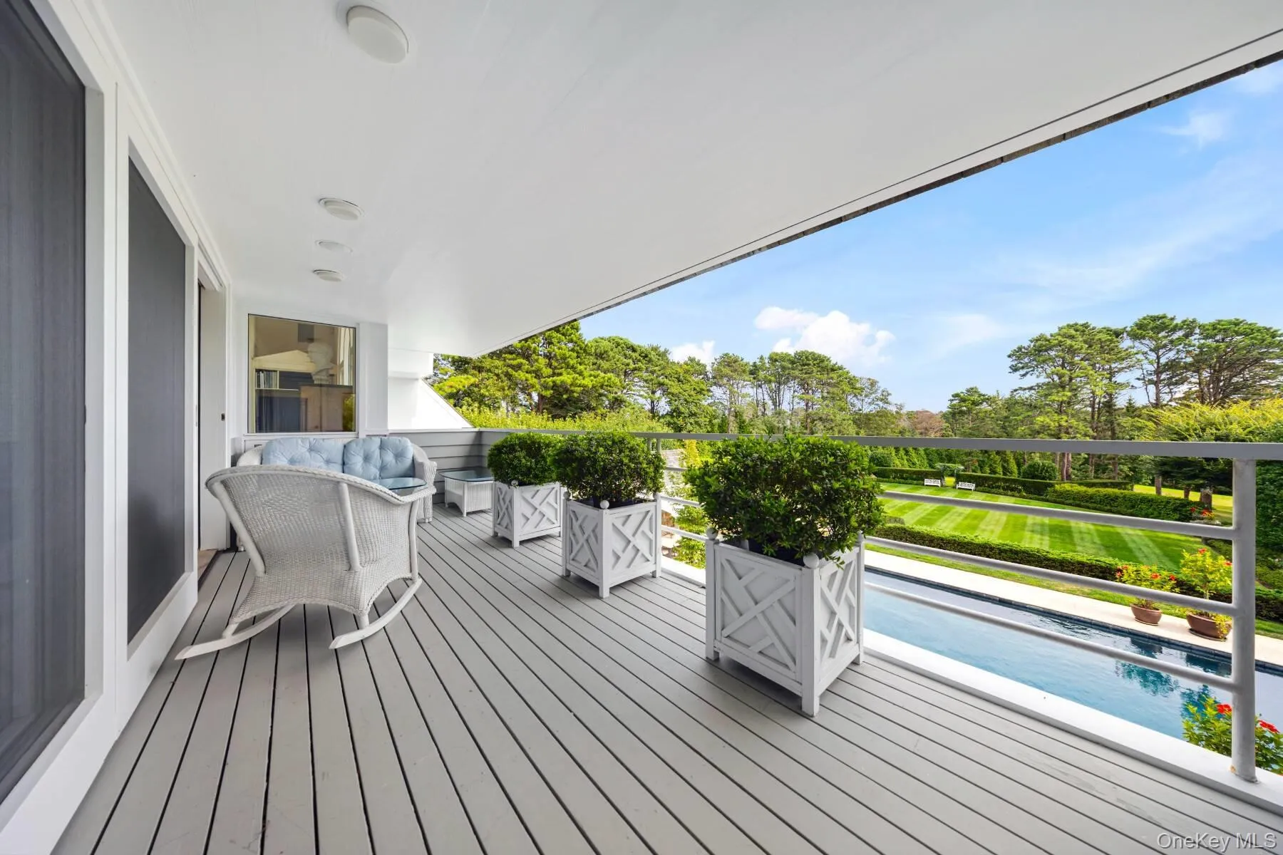 Wooden deck featuring an outdoor pool, view of scattered trees, and grilling area Wooden deck featuring an outdoor pool, view of scattered trees, and grilling area