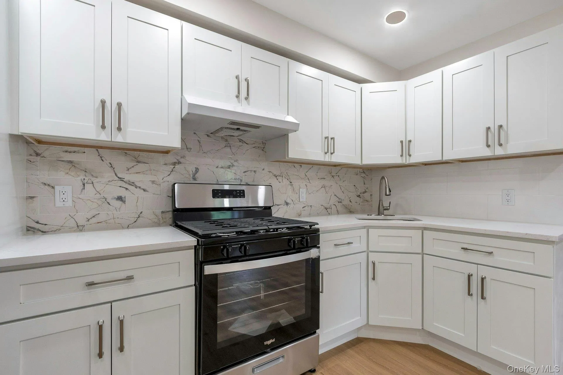 Kitchen featuring gas stove, white cabinetry, decorative backsplash, and under cabinet range hood Kitchen featuring gas stove, white cabinetry, decorative backsplash, and under cabinet range hood