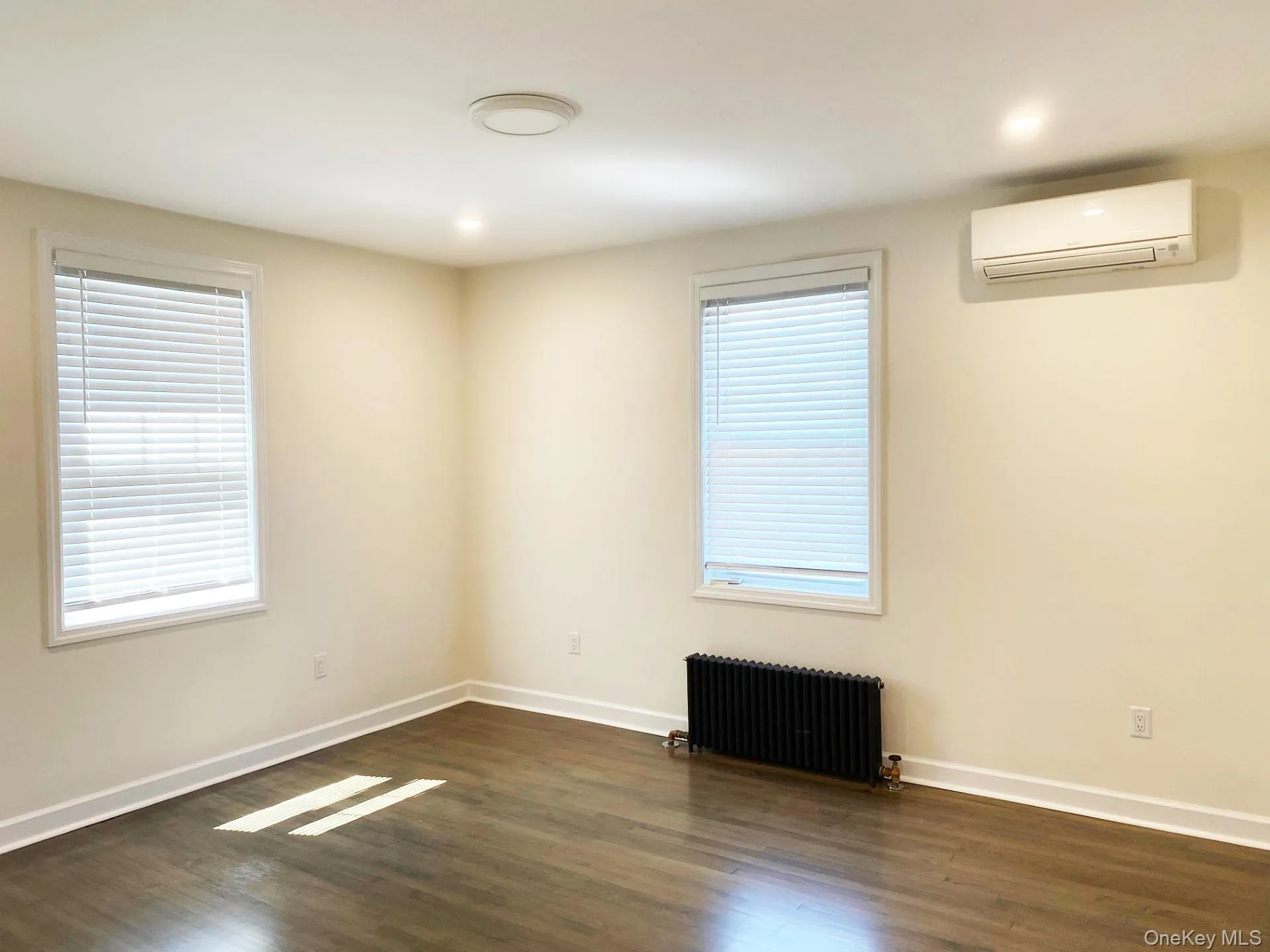 Spare room featuring radiator heating unit, dark wood-style flooring, and an AC wall unit Spare room featuring radiator heating unit, dark wood-style flooring, and an AC wall unit
