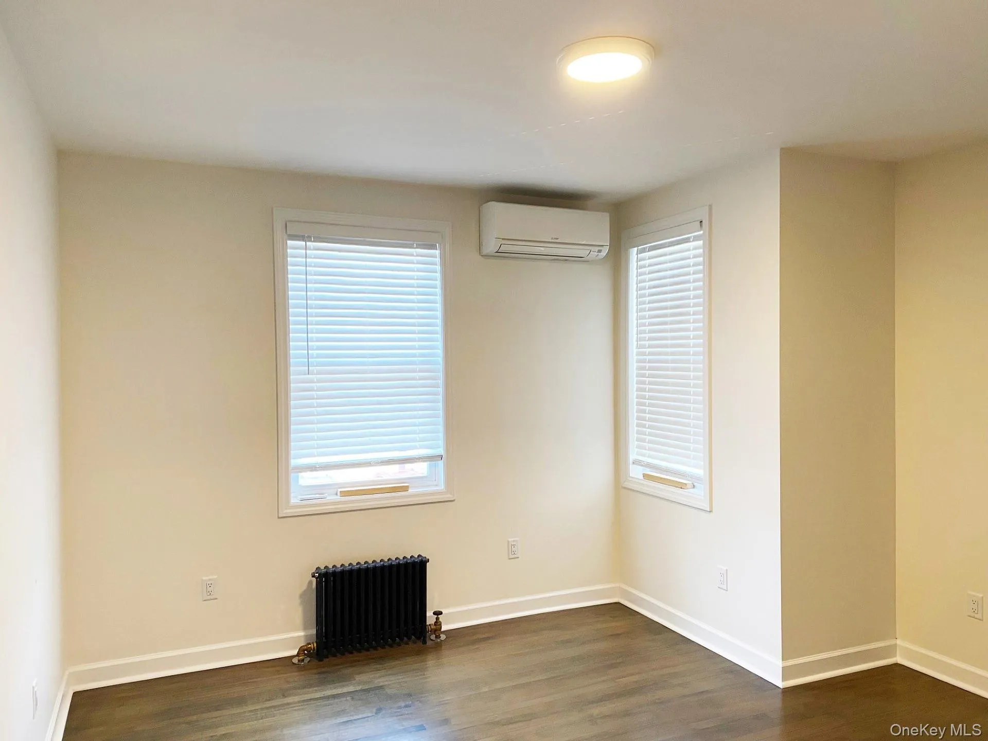 Unfurnished room with radiator heating unit, dark wood-type flooring, and an AC wall unit Unfurnished room with radiator heating unit, dark wood-type flooring, and an AC wall unit
