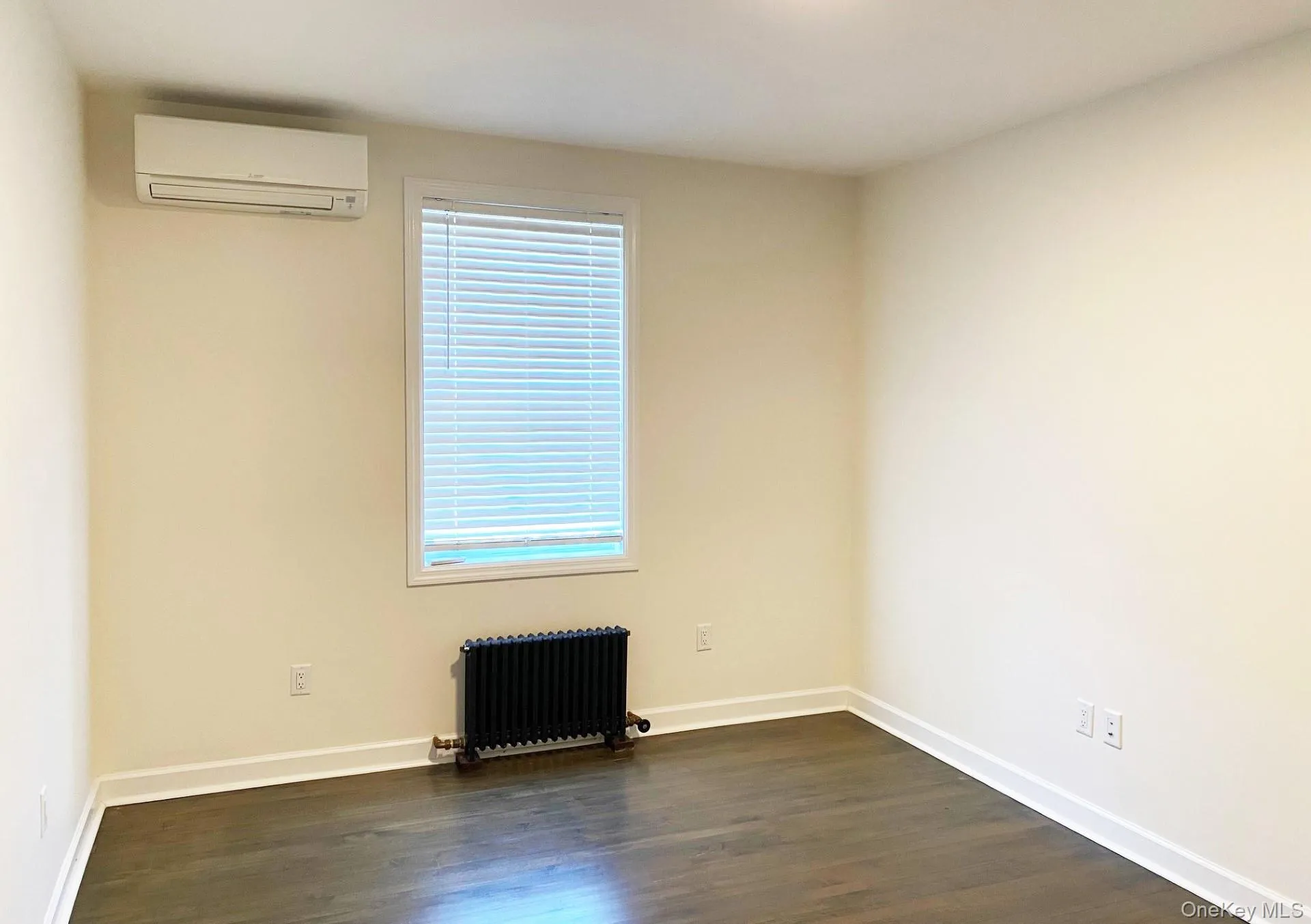 Unfurnished room featuring radiator, dark wood-style floors, and a wall mounted AC Unfurnished room featuring radiator, dark wood-style floors, and a wall mounted AC