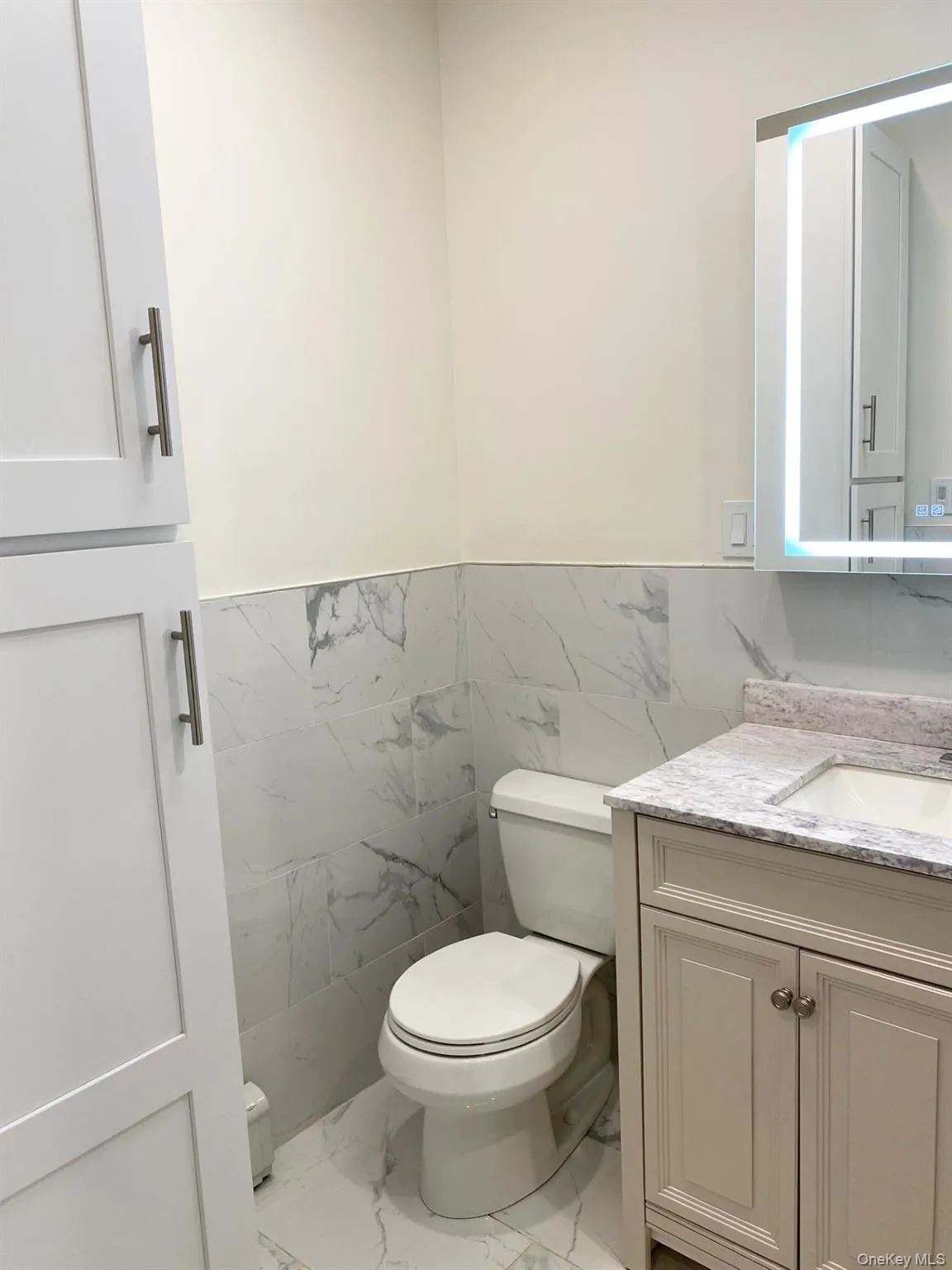 Half bath featuring vanity, light marble finish floors, tile walls, and a wainscoted wall Half bath featuring vanity, light marble finish floors, tile walls, and a wainscoted wall