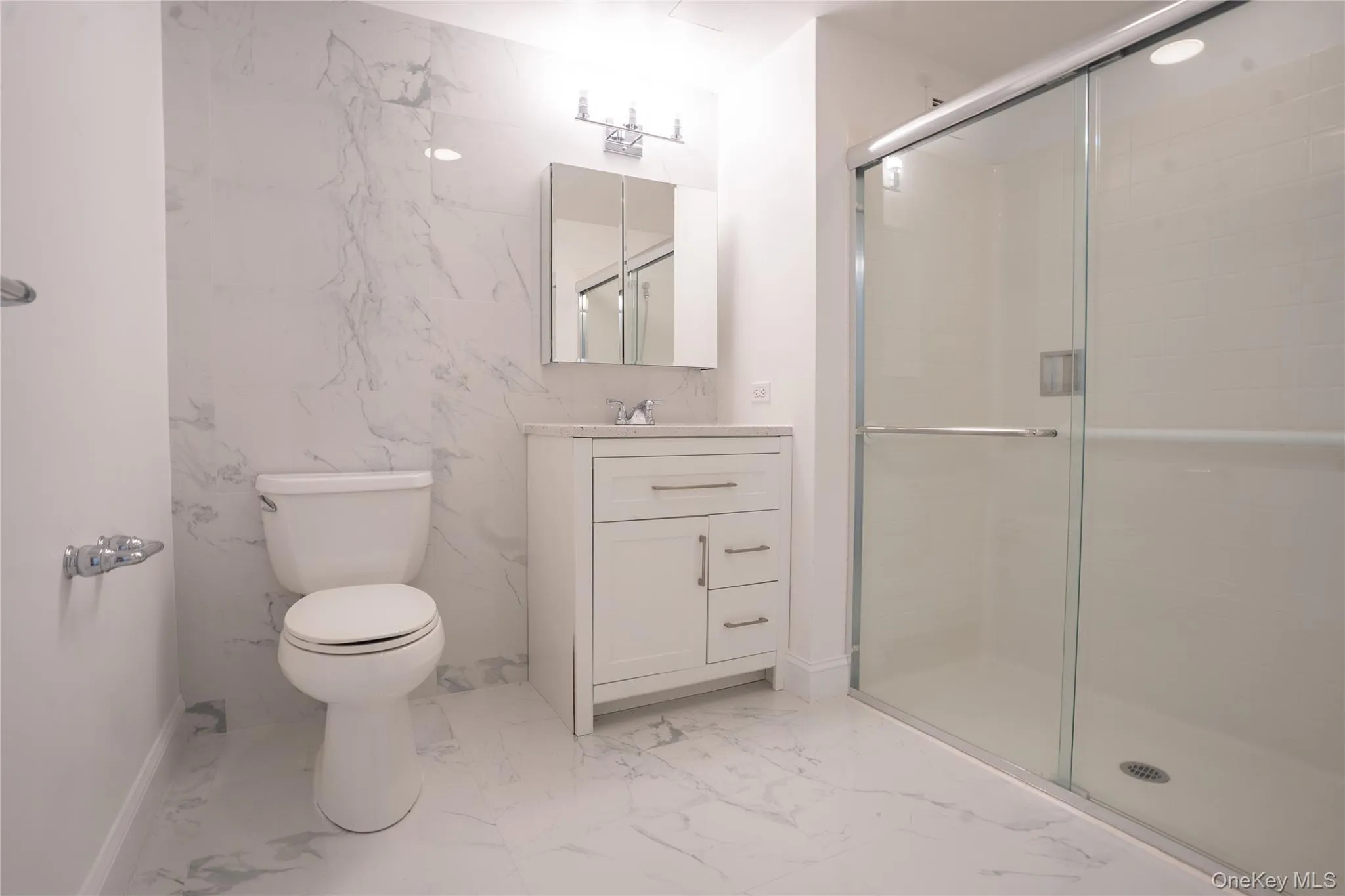 Ensuite Bathroom featuring a shower, vanity, light marble finish floors, and tile walls Ensuite Bathroom featuring a shower, vanity, light marble finish floors, and tile walls