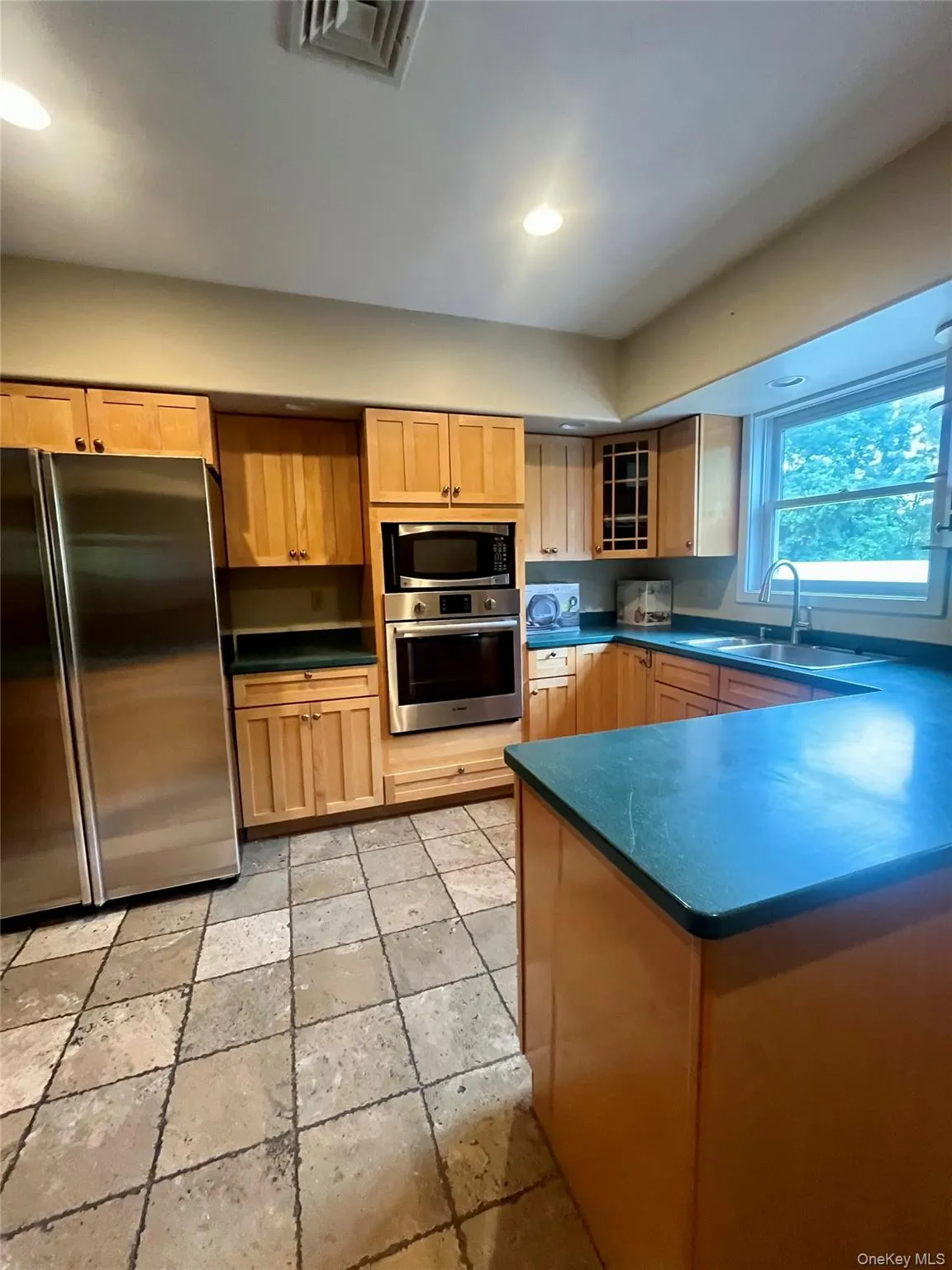 Kitchen featuring appliances with stainless steel finishes, dark countertops, glass insert cabinets, recessed lighting, and light brown cabinets Kitchen featuring appliances with stainless steel finishes, dark countertops, glass insert cabinets, recessed lighting, and light brown cabinets
