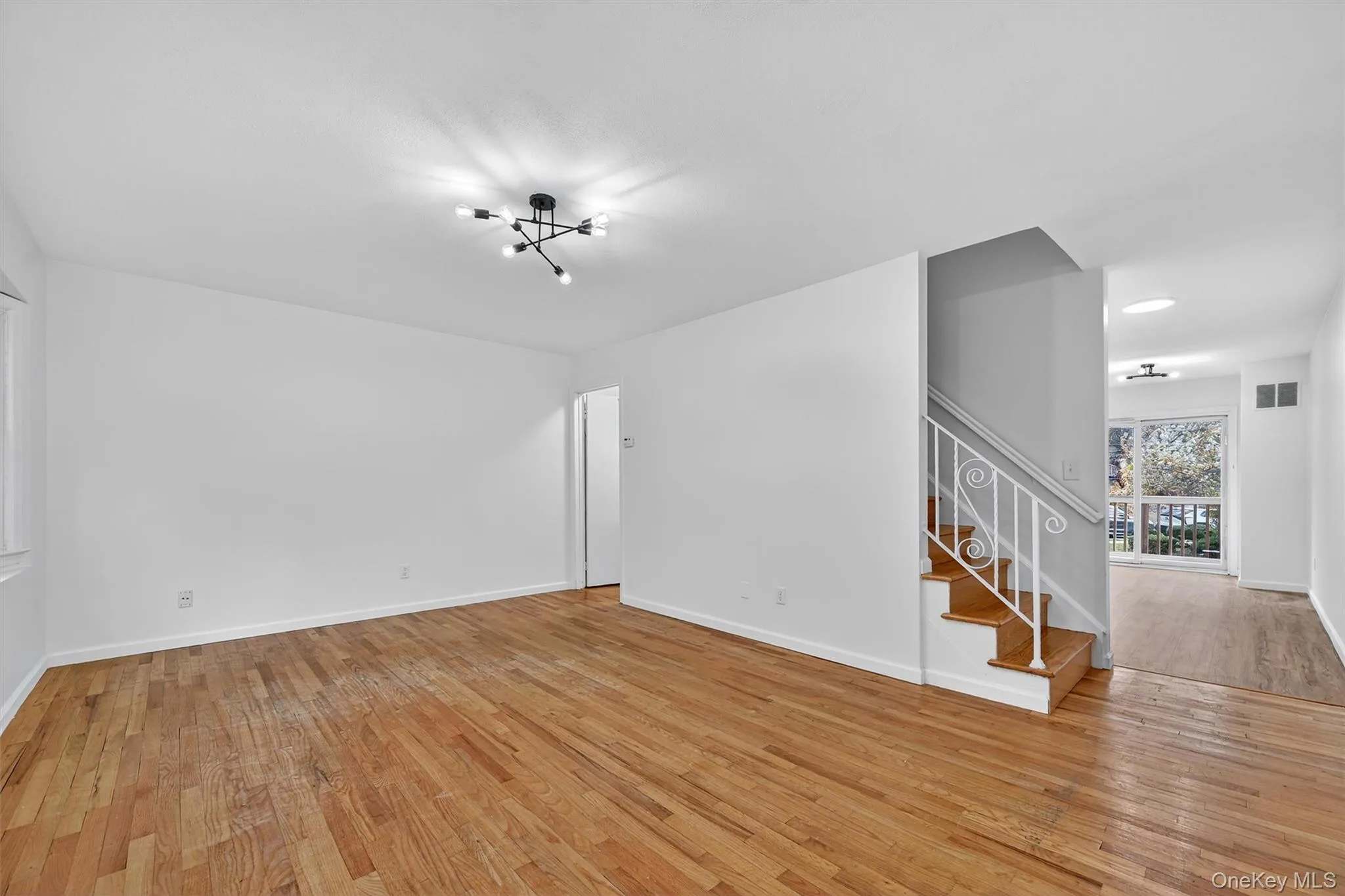Unfurnished living room featuring light wood finished floors, stairs, and a chandelier Unfurnished living room featuring light wood finished floors, stairs, and a chandelier