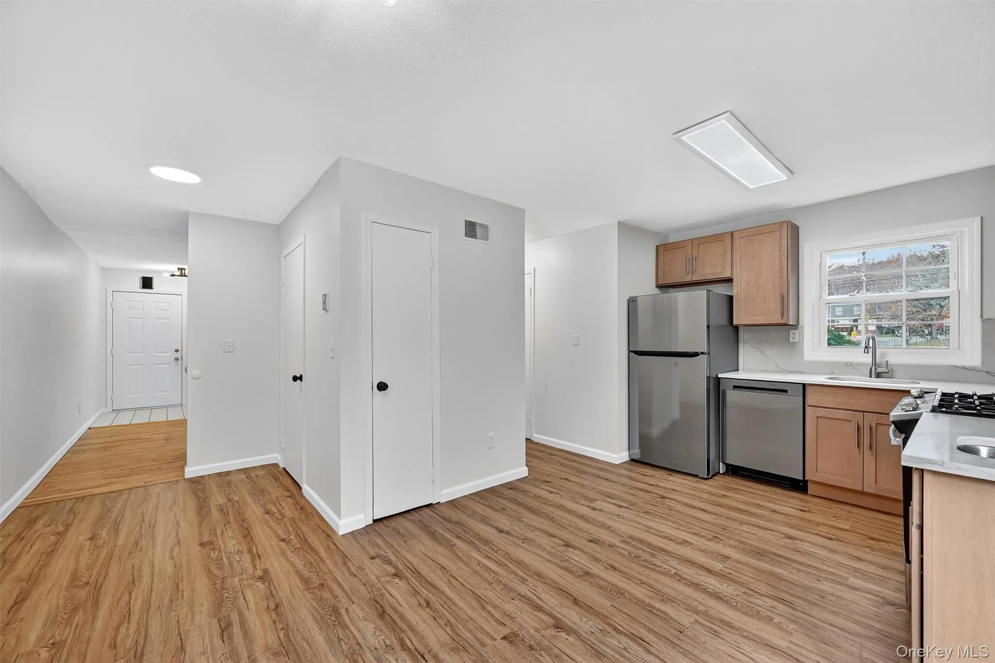 Kitchen with light wood-type flooring, stainless steel appliances, light stone counters, brown cabinetry, and backsplash Kitchen with light wood-type flooring, stainless steel appliances, light stone counters, brown cabinetry, and backsplash