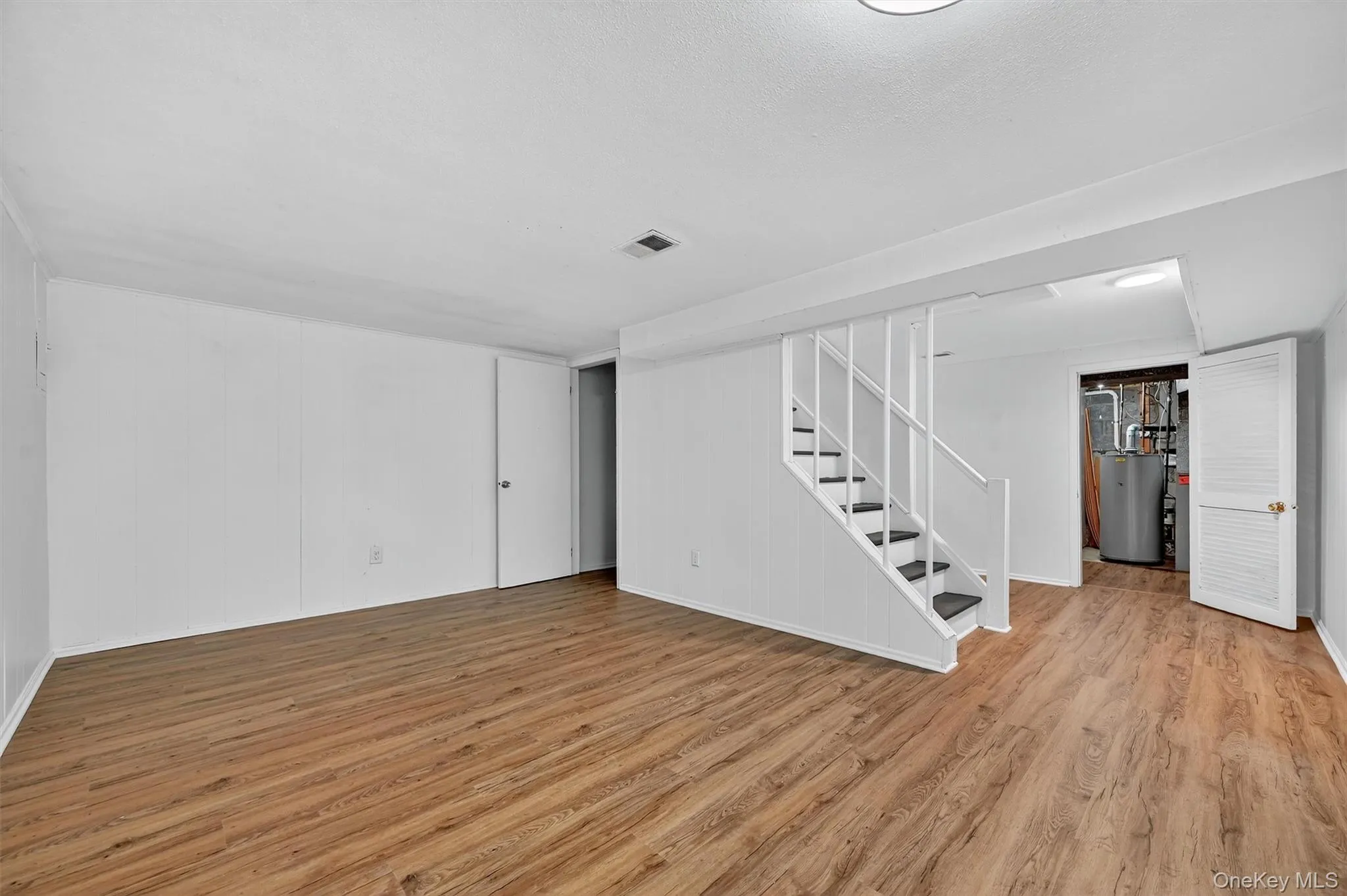Finished below grade area featuring light wood-style flooring, stairs, and water heater Finished below grade area featuring light wood-style flooring, stairs, and water heater