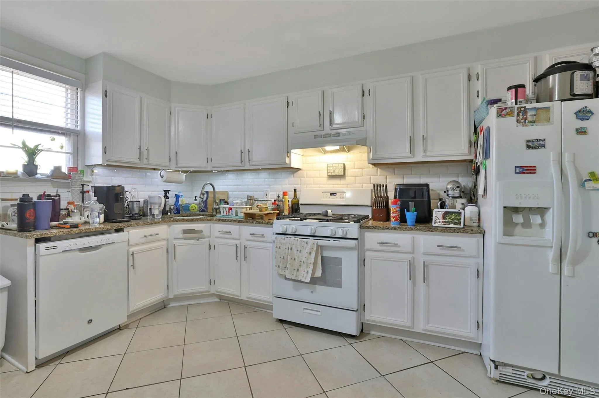 Kitchen with white appliances, white cabinets, tasteful backsplash, light tile patterned floors, and under cabinet range hood Kitchen with white appliances, white cabinets, tasteful backsplash, light tile patterned floors, and under cabinet range hood