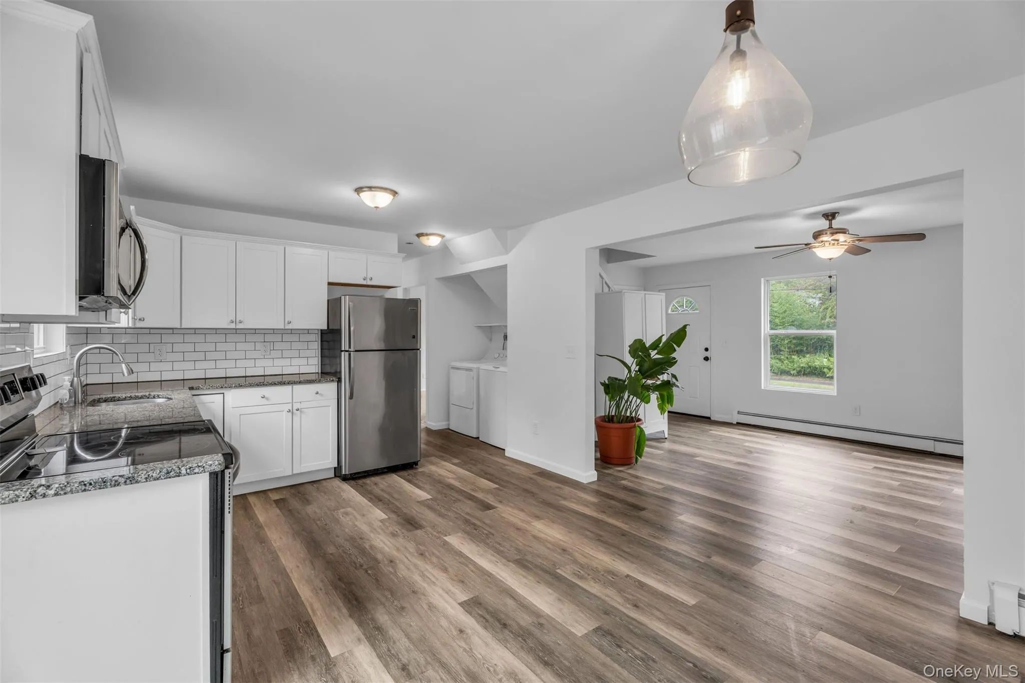 Kitchen with stainless steel appliances, white cabinetry, tasteful backsplash, dark wood-style floors, and baseboard heating Kitchen with stainless steel appliances, white cabinetry, tasteful backsplash, dark wood-style floors, and baseboard heating