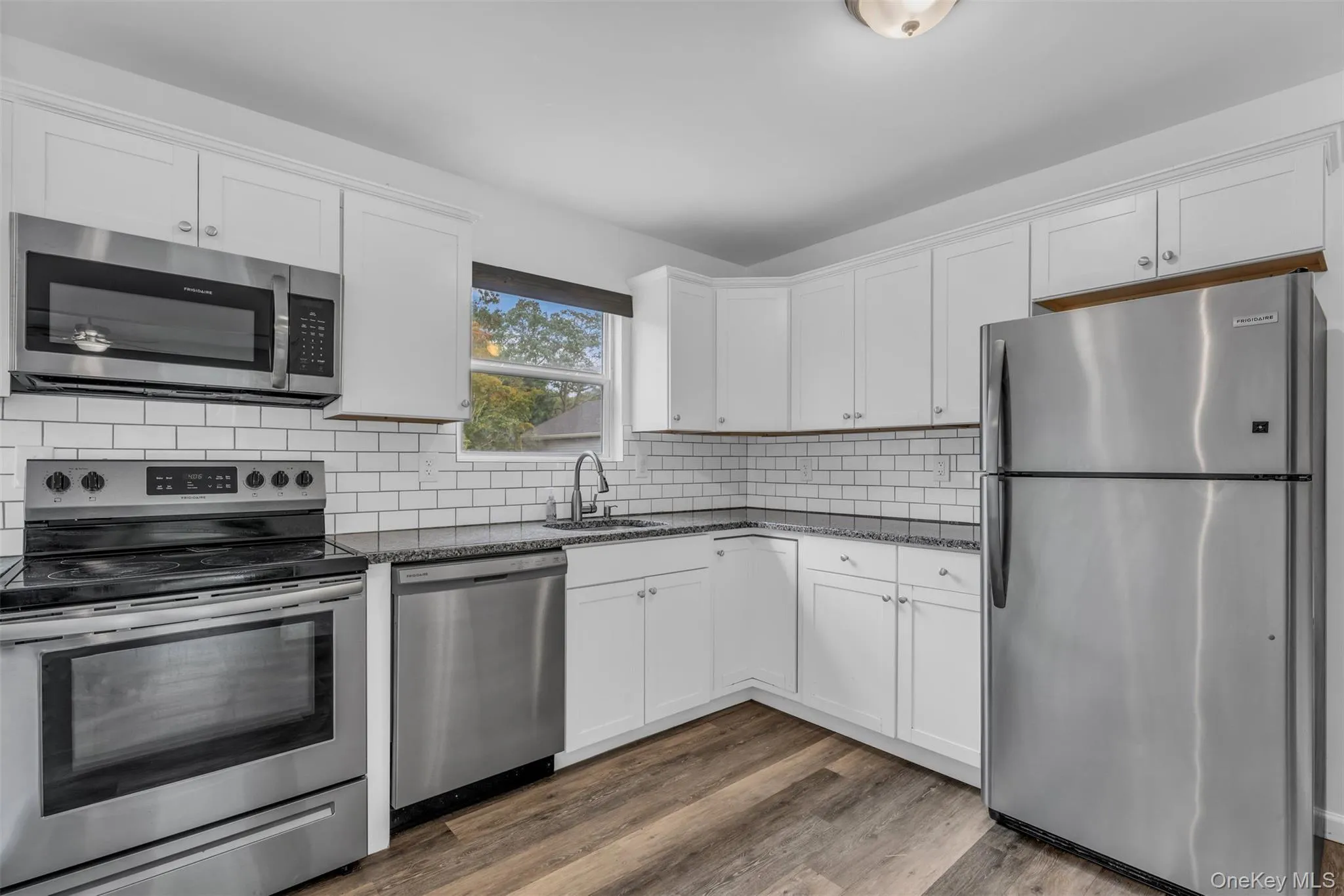 Kitchen featuring stainless steel appliances, white cabinetry, dark wood-style floors, and decorative backsplash Kitchen featuring stainless steel appliances, white cabinetry, dark wood-style floors, and decorative backsplash