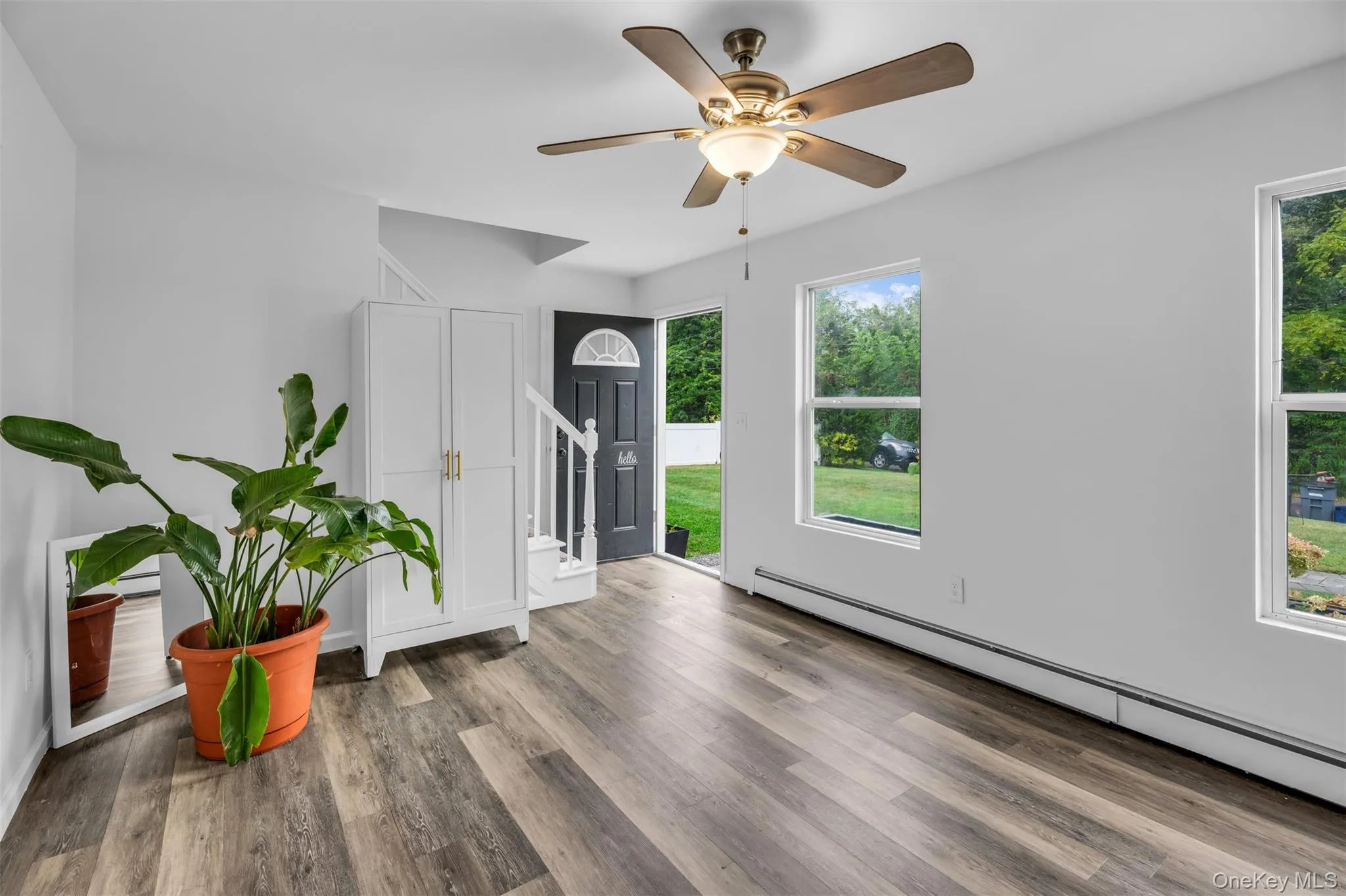 Entryway featuring baseboard heating, wood finished floors, ceiling fan, and stairway Entryway featuring baseboard heating, wood finished floors, ceiling fan, and stairway